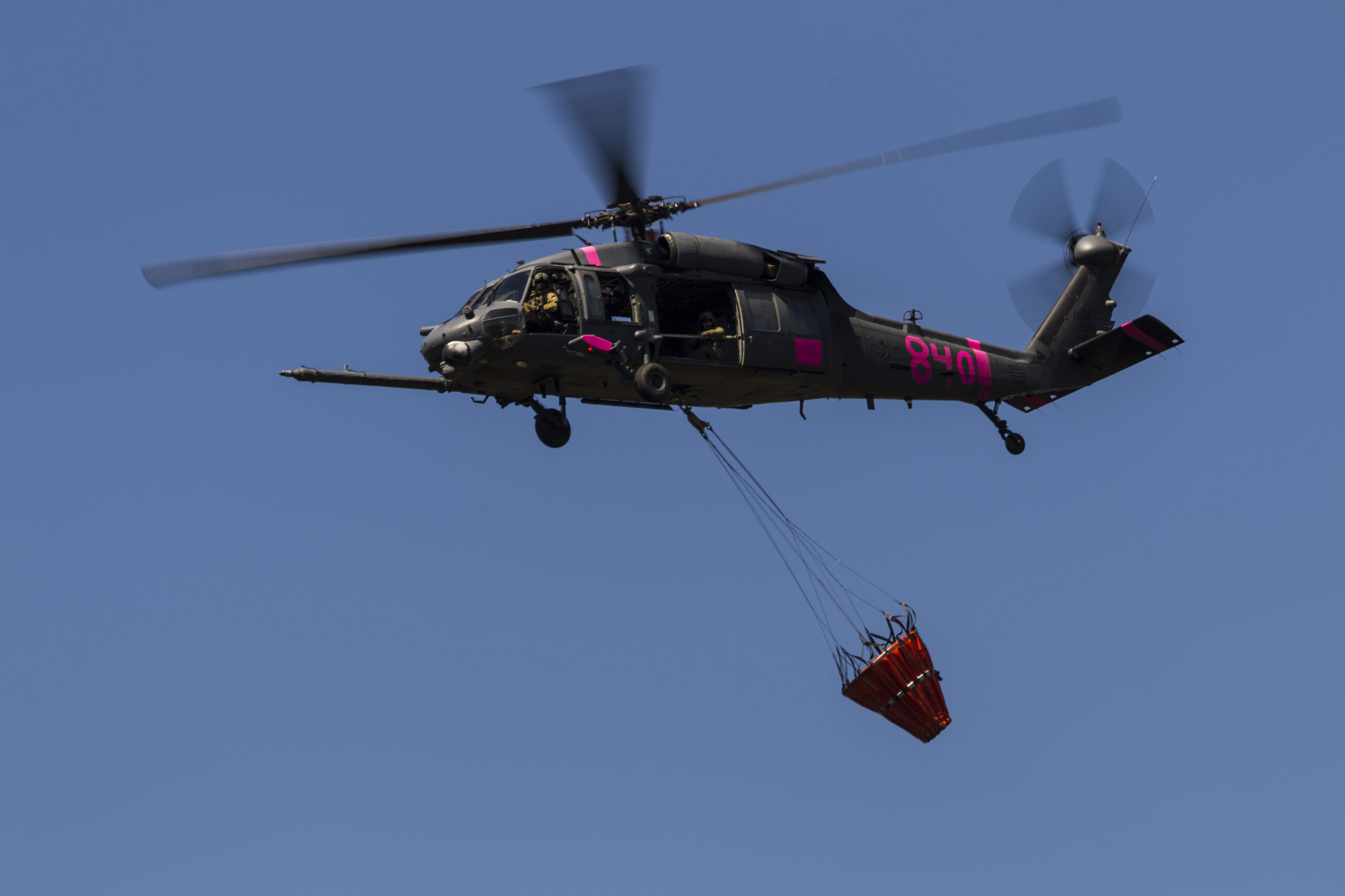 A photo of a Cal Guard firehawk helicopter with a bucket of water to fight wildfires