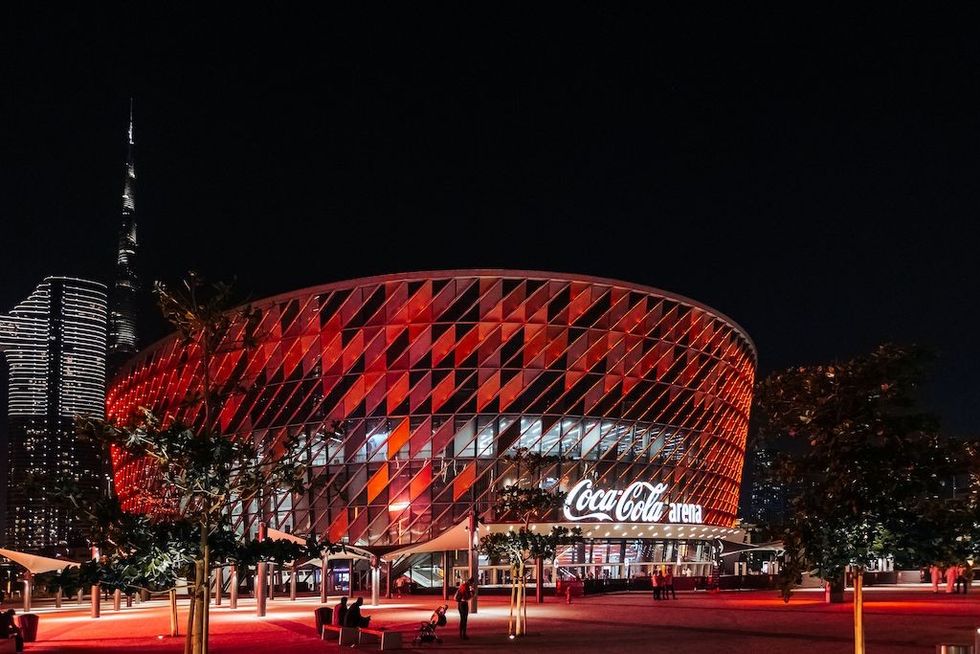 Coca-Cola Arena at night, lit in red, with a city skyline in the background.