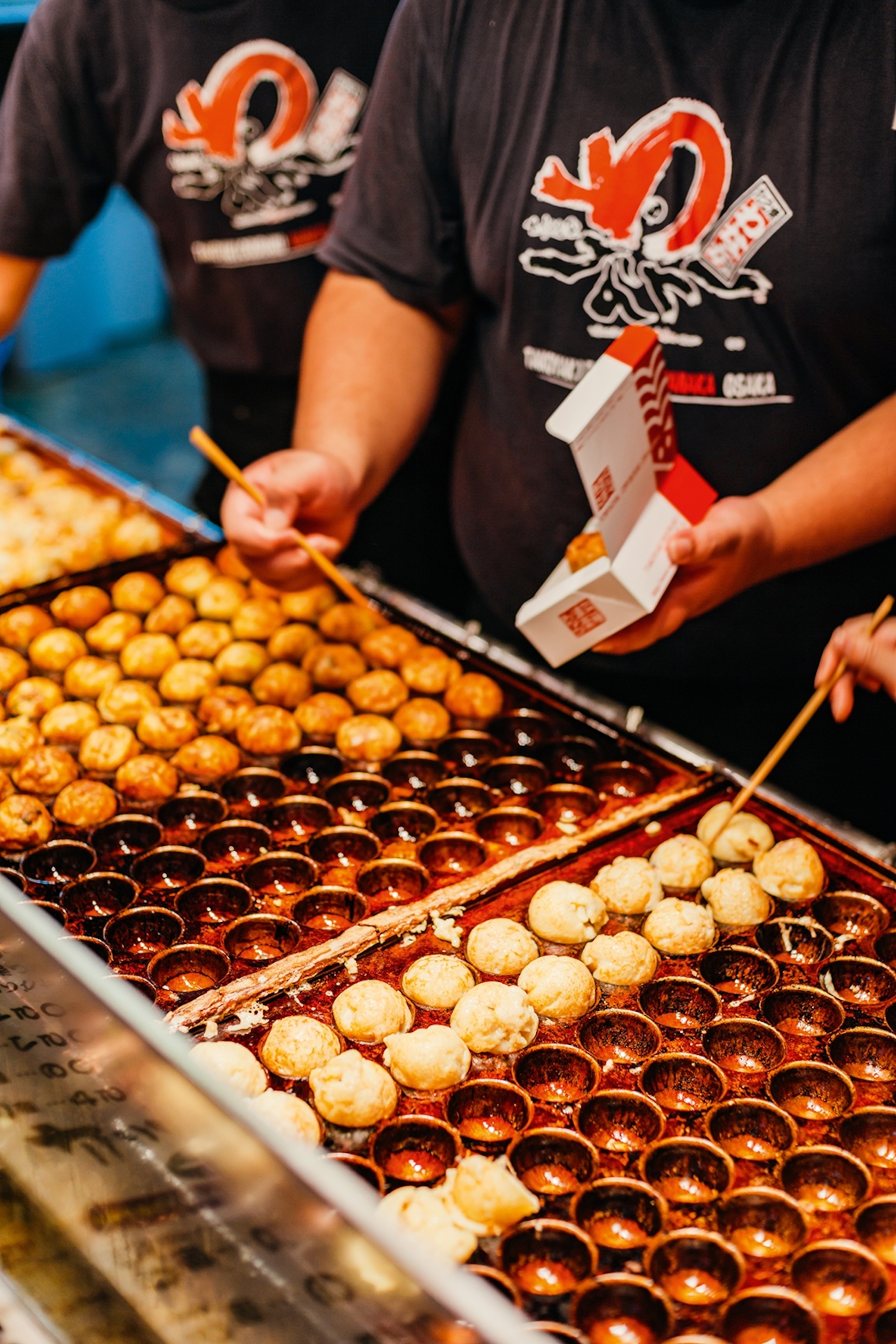 A close-up of a man flipping little dough balls on a suitable, bubble-wrap-like griddle.