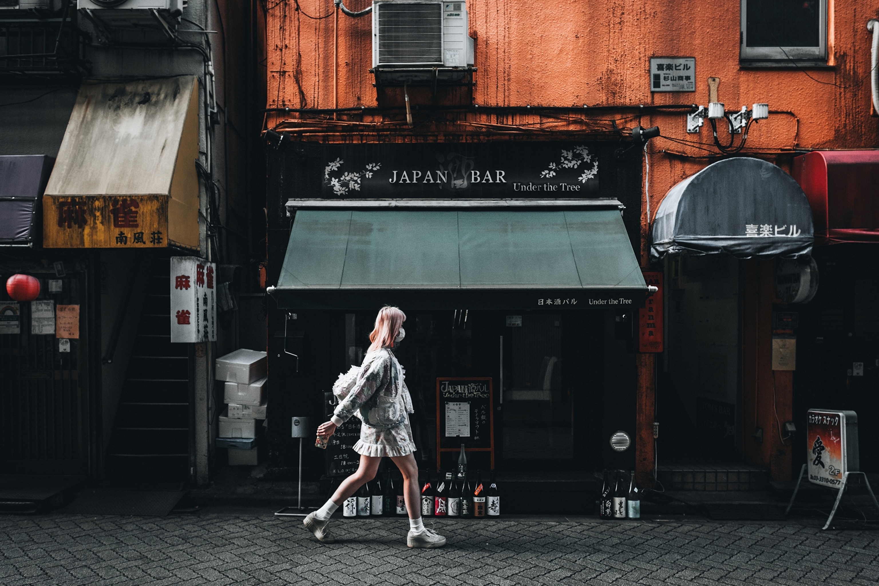 A girl dressed in frilly clothes and platform sneakers walks past a Japanese street bar.