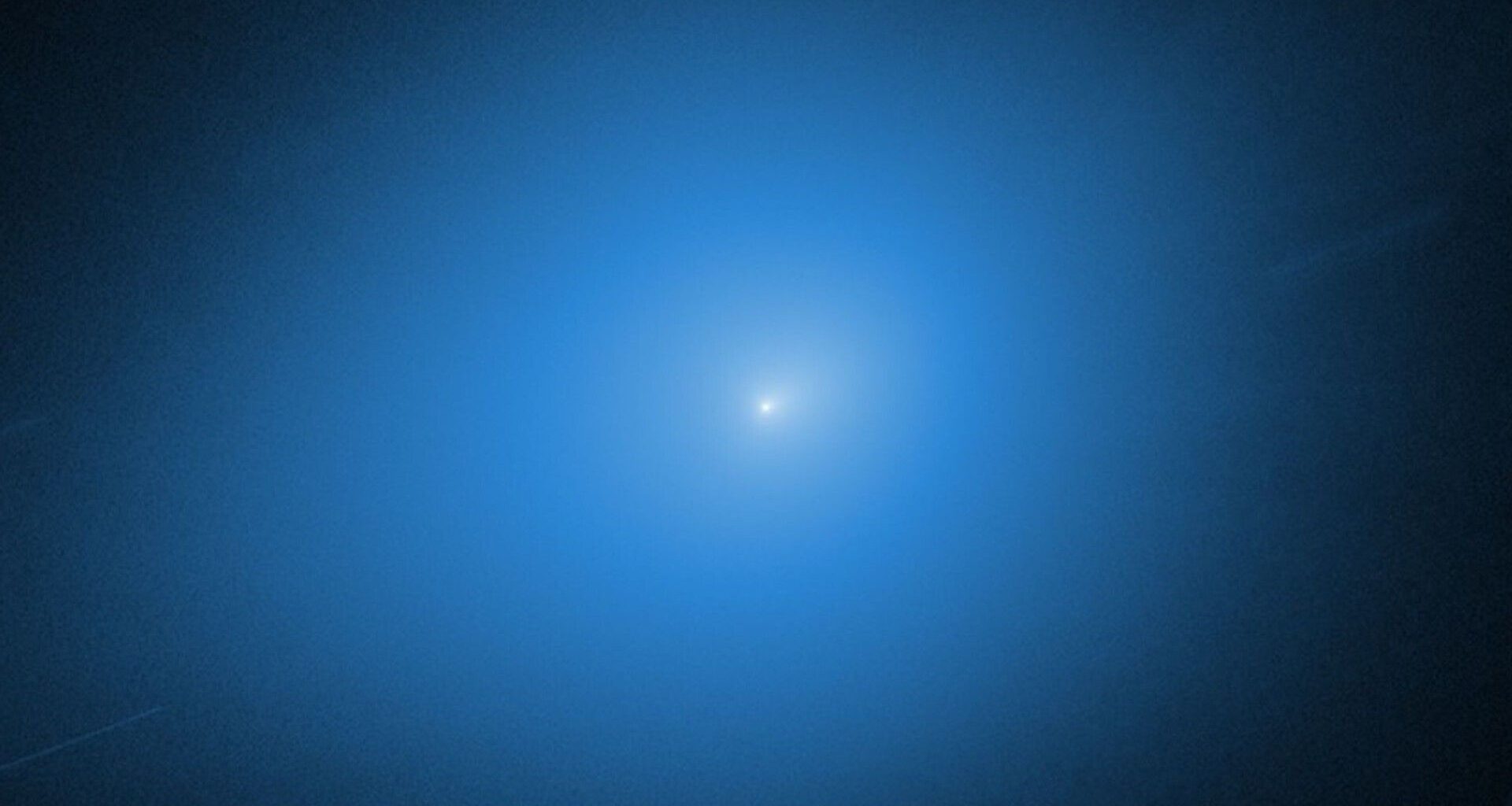 A white light of the comet 3I/ATLAS is surrounded by a blue glow against a black background
