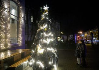 People stand near a Christmas tree dedicated to Ukraine’s energy workers in downtown Kyiv on December 22, 2025. Made from utility workers’ uniforms, the installation honors those keeping the country’s power grid running amid sustained Russian attacks.