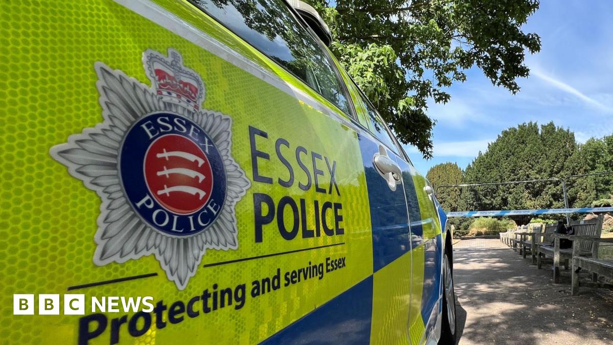 An Essex Police car parked in front of police tape. There are trees and bushes in front of the car.