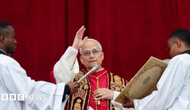 Pope Leo speaking into a microphone during his Christmas address and holding his hand in the air