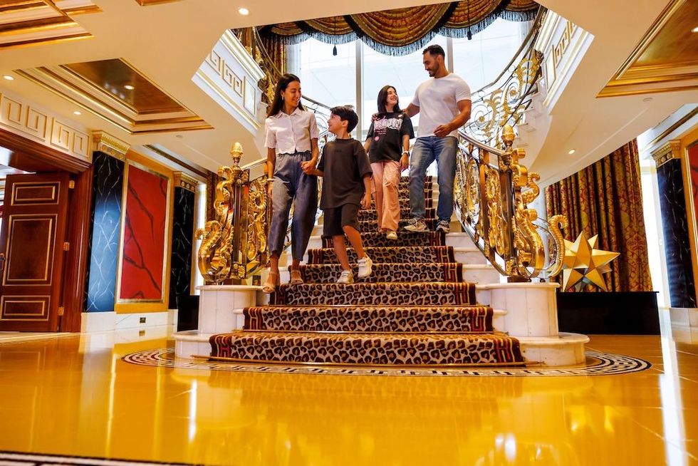 Family descending ornate staircase in luxury interior with gold accents.