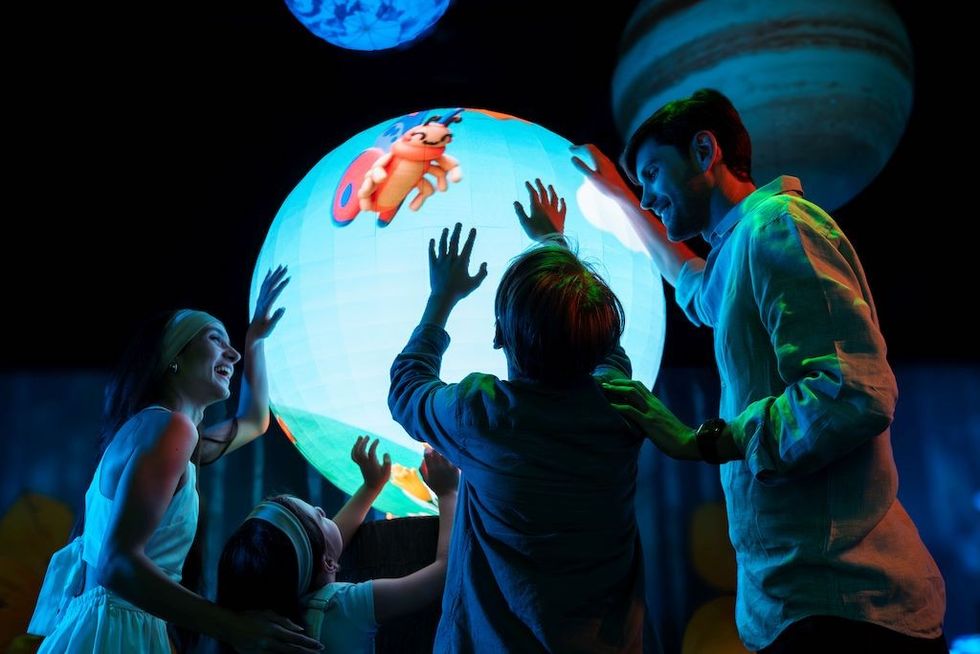 Family interacting with a glowing globe displaying a colorful insect in a dark room.