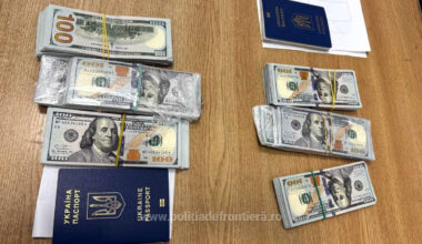 60.000 de dolari în hârtii de câte 100 de dolari, așezate pe o masă din lemn maro, lângă două pașapoarte de Ucraina