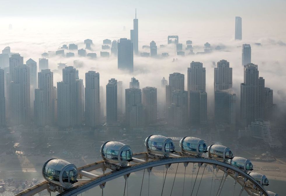Ferris wheel above a foggy city skyline with tall buildings in the background.