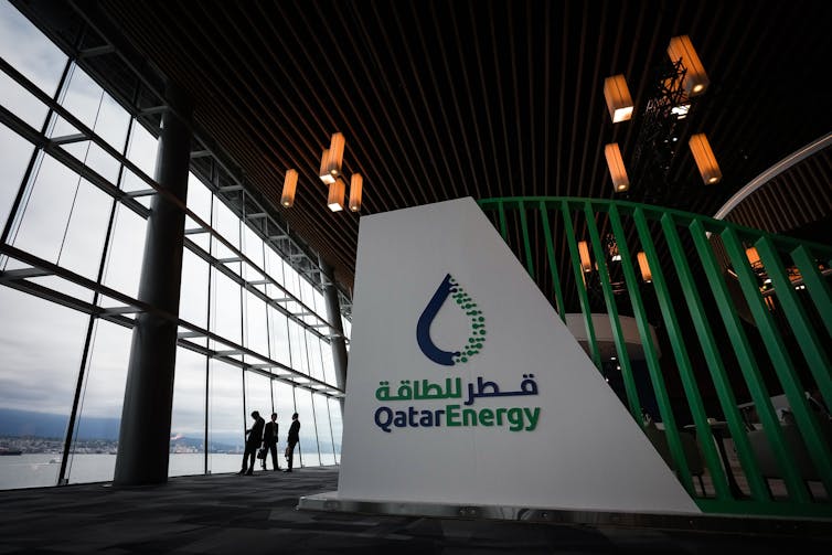 A wall of a booth with Qatar Energy written on it stads in a large hall.