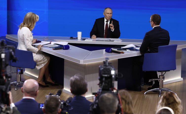 Vladimir Putin appears with two TV presenters at a press conference.