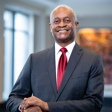 Raphael Bostic standing with hands folded in front of a window and artwork