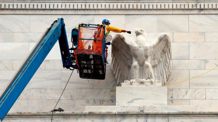 A construction worker in a lift paints a large eagle sculpture on the exterior of the Marriner S. Eccles Federal Reserve Board Building.