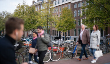 People walk across a bridge over the Keizersgracht canal in Amsterdam with bicycles parked nearby.