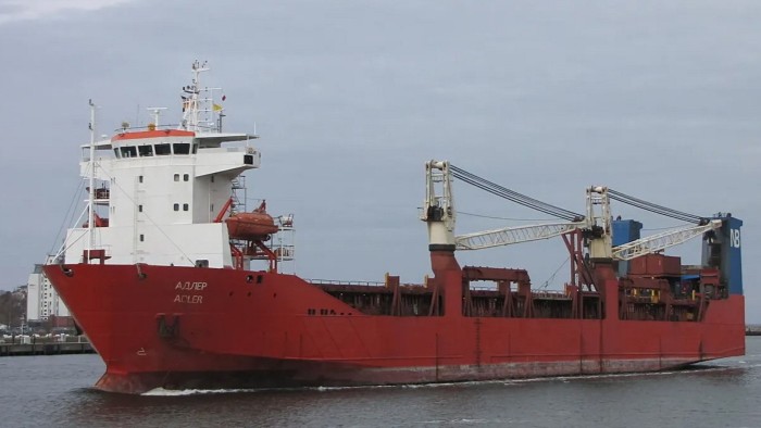 The Russian cargo ship Adler sails on the water, showing a red hull, white superstructure, and onboard cranes.
