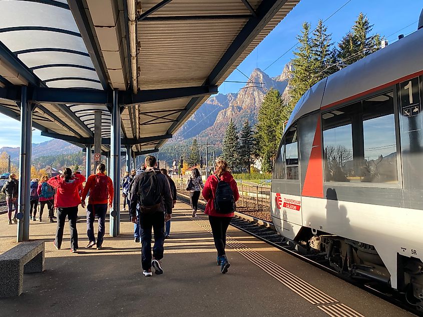 Passengers disembarking from a train at a sunny mountain town station 