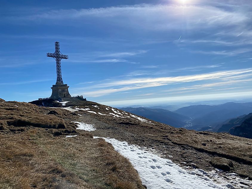 A trail leads to large steel cross atop a sunny mountain