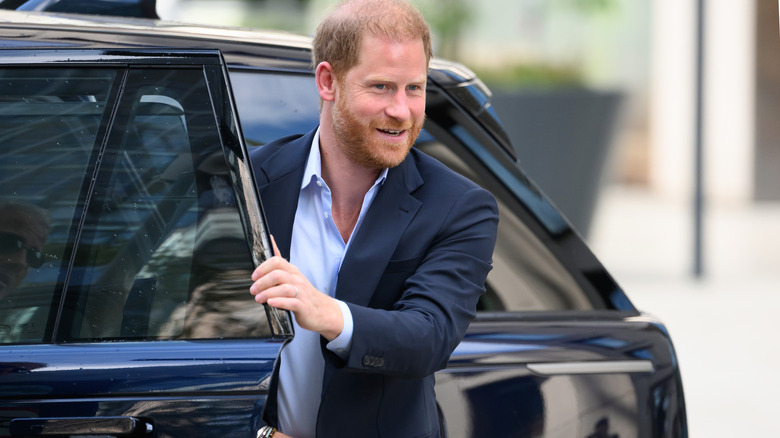 Prince Harry emerges from a black car smiling
