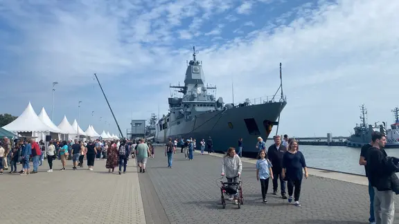 Besucher laufen beim Tag der offenen Tür auf dem Marinestützpunkt in Wilhelmshaven an einem Kriegsschiff vorbei.