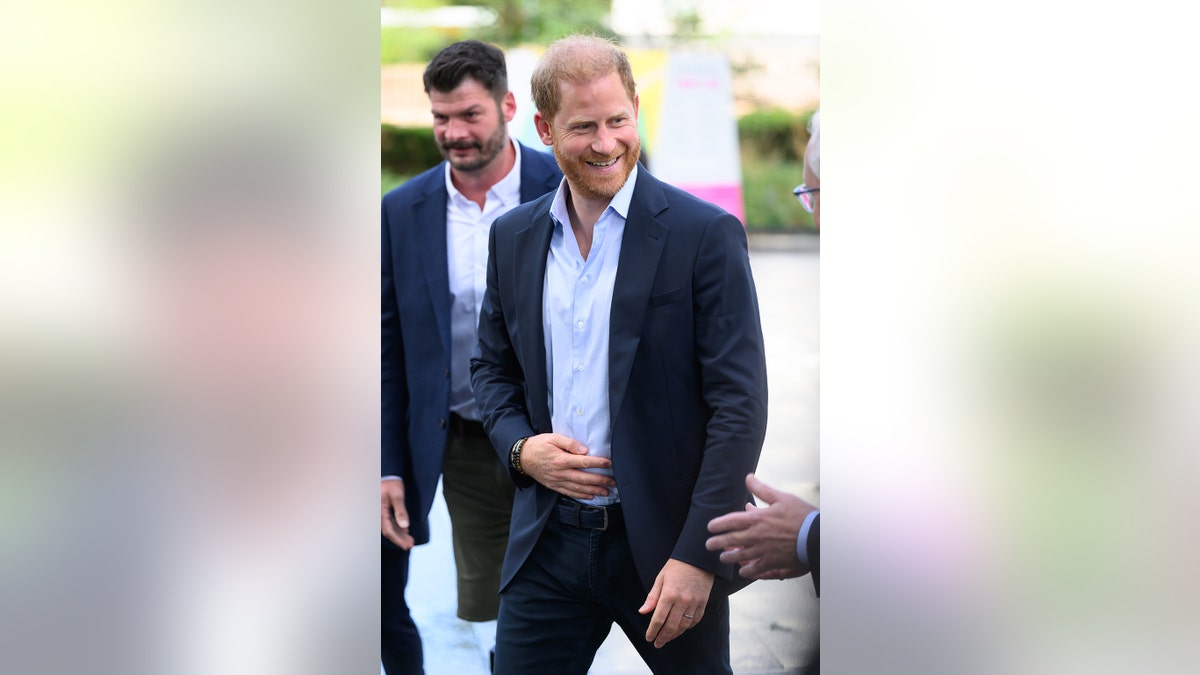 Prince Harry smiling and walking in a dark blue suit.