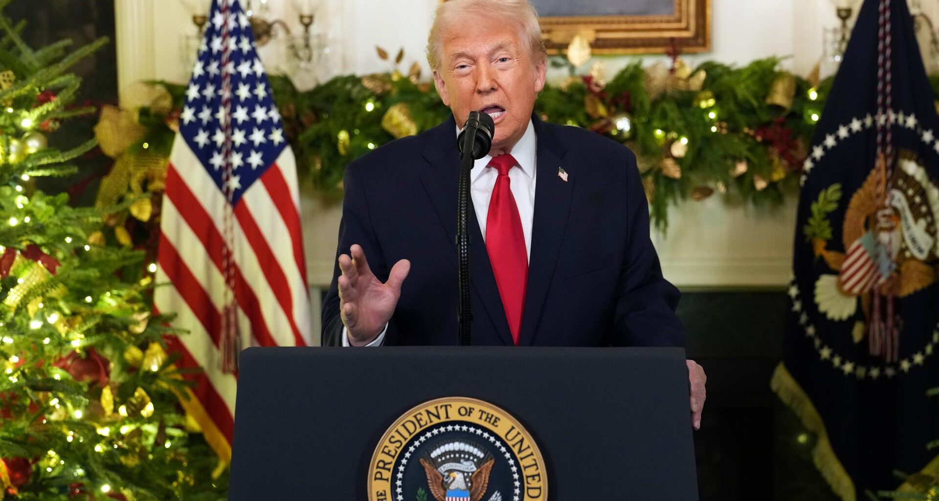 Donald Trump steht an einem Redepult und spricht in Richtung Kamera. Im Hintergrund ist eine US-Flagge zu sehen.