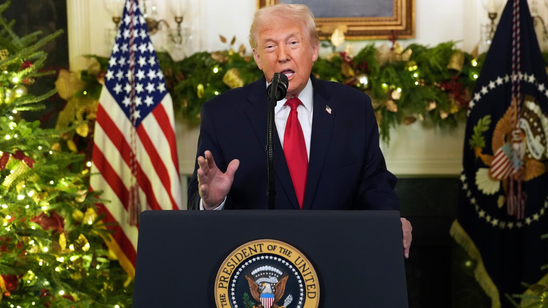 Donald Trump steht an einem Redepult und spricht in Richtung Kamera. Im Hintergrund ist eine US-Flagge zu sehen.