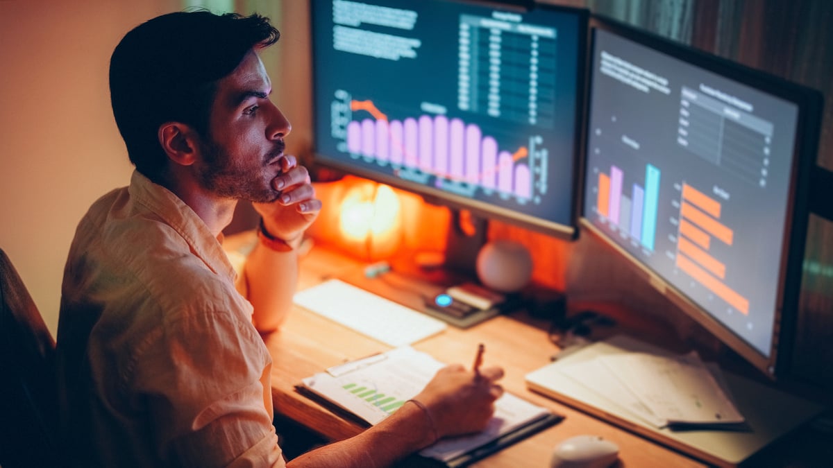Man takes notes as he looks at computer screen showing investments.