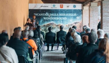A man addresses a small crowd seated outside