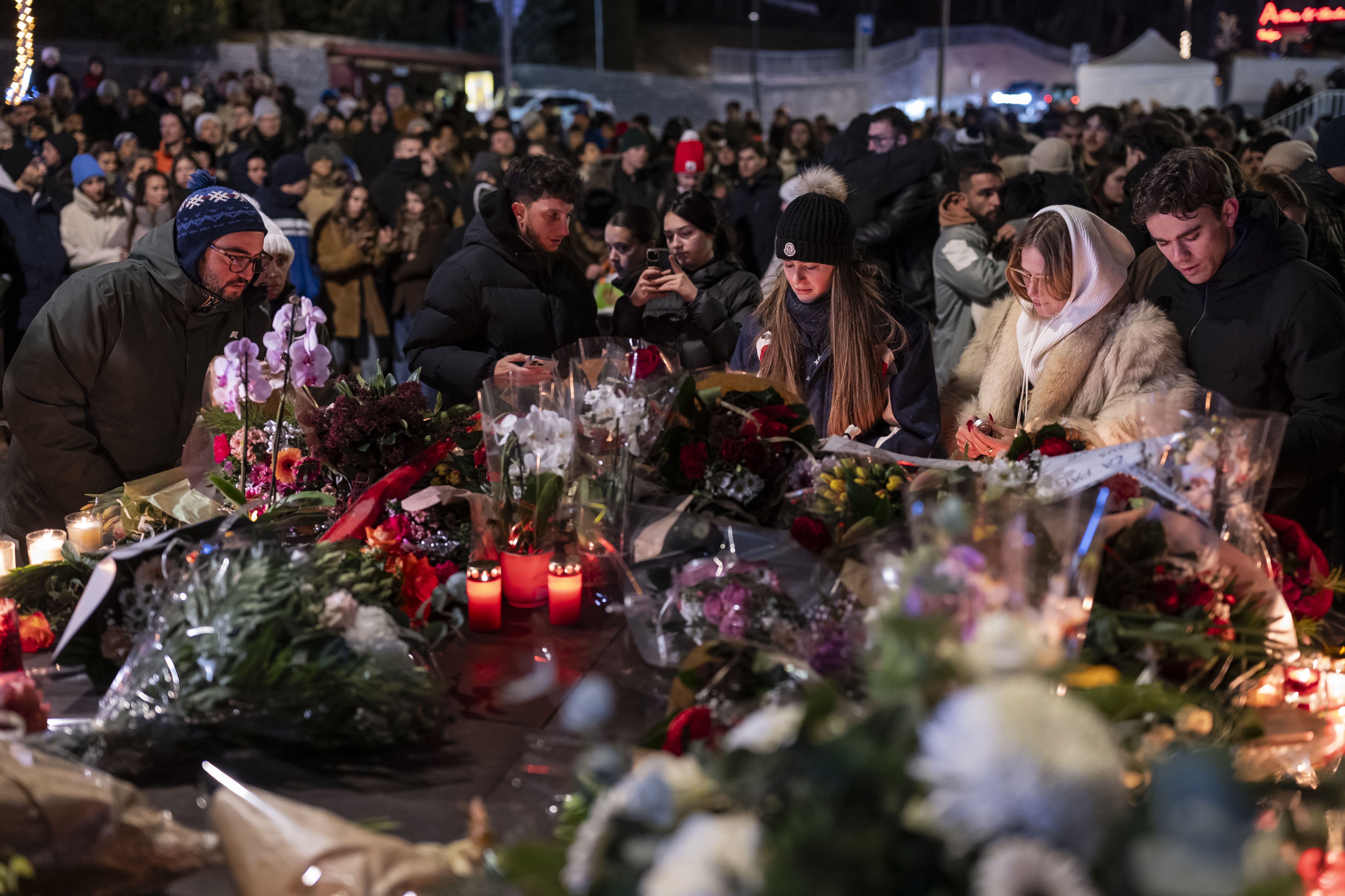 Mourners gather at night to lay flowers and light candles to remember victims of a fire at Le Constellation bar and lounge.