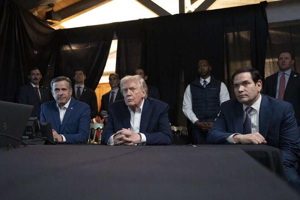 Donald Trump, John Ratcliffe, and Marco Rubio sit at a table with other men standing behind them.