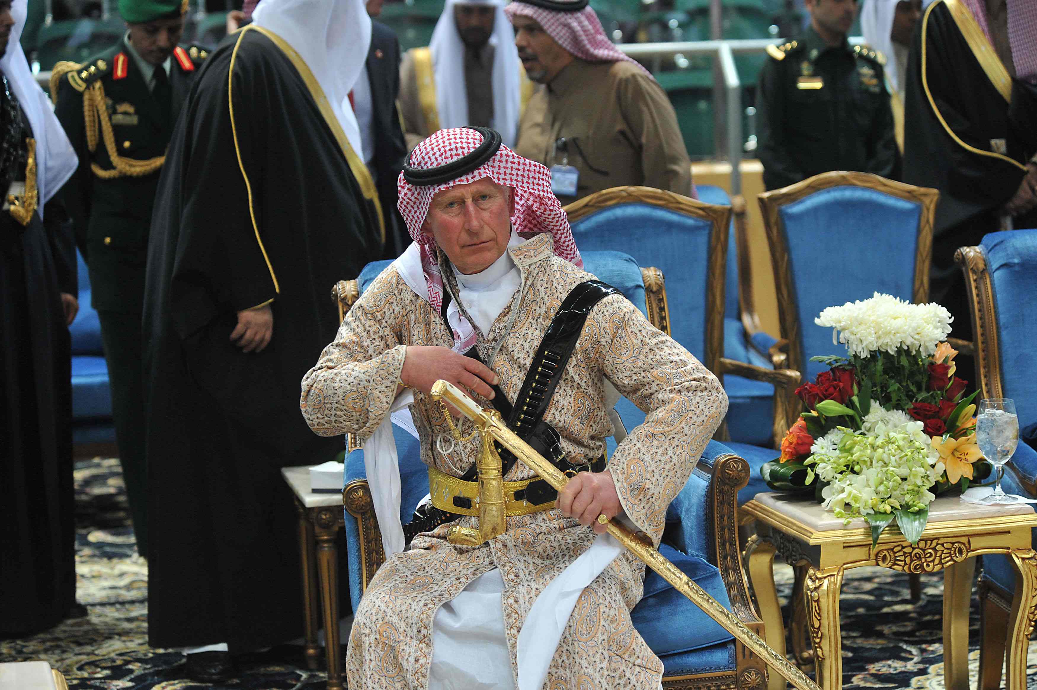 Prince Charles in traditional Saudi uniform, seated, holding a gold sword.