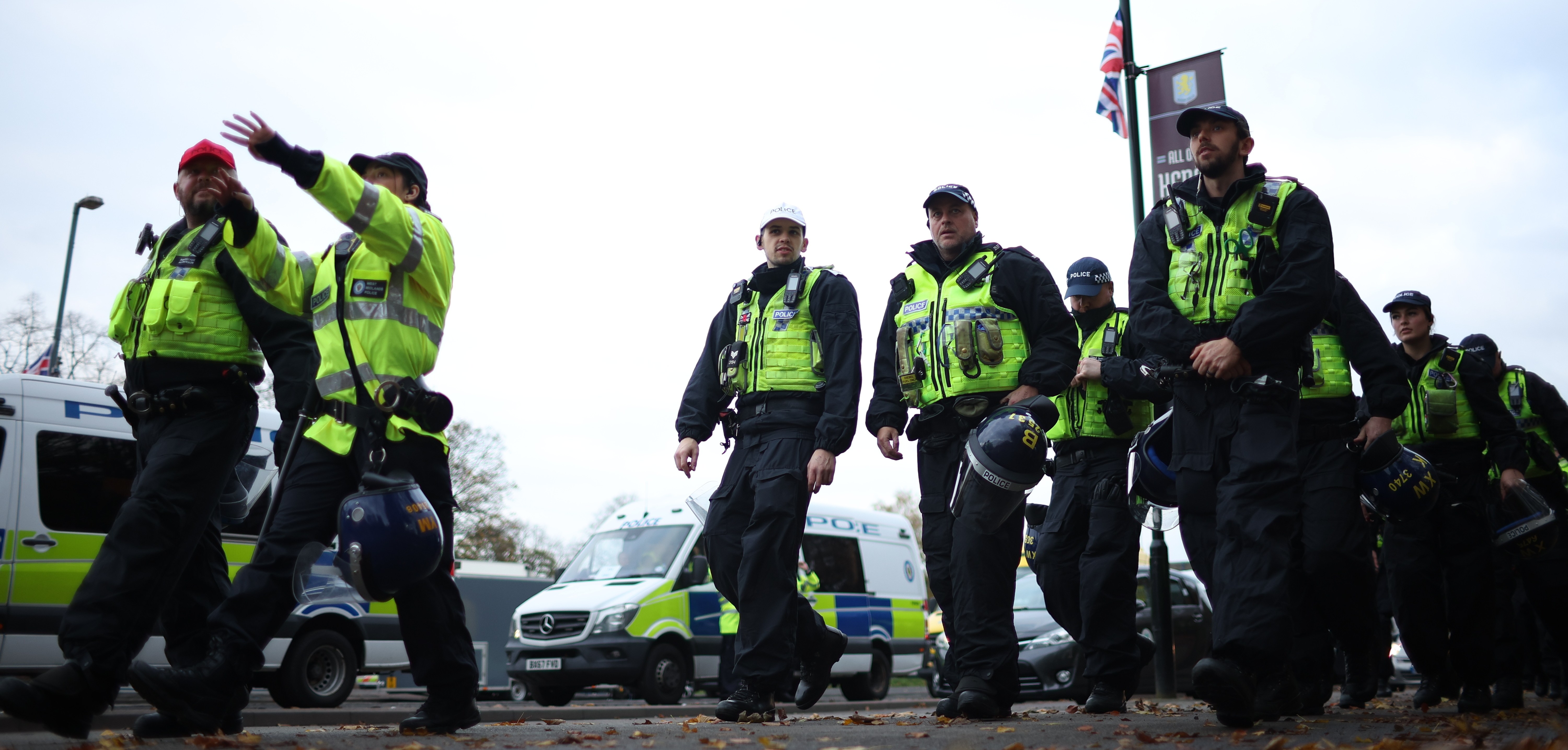 Police officers with protective vests and helmets walk down a street.