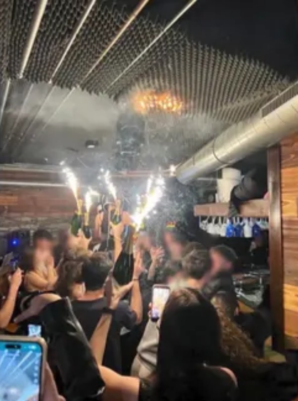 A fire starting on the ceiling of a bar as people celebrate with sparkling champagne bottles.