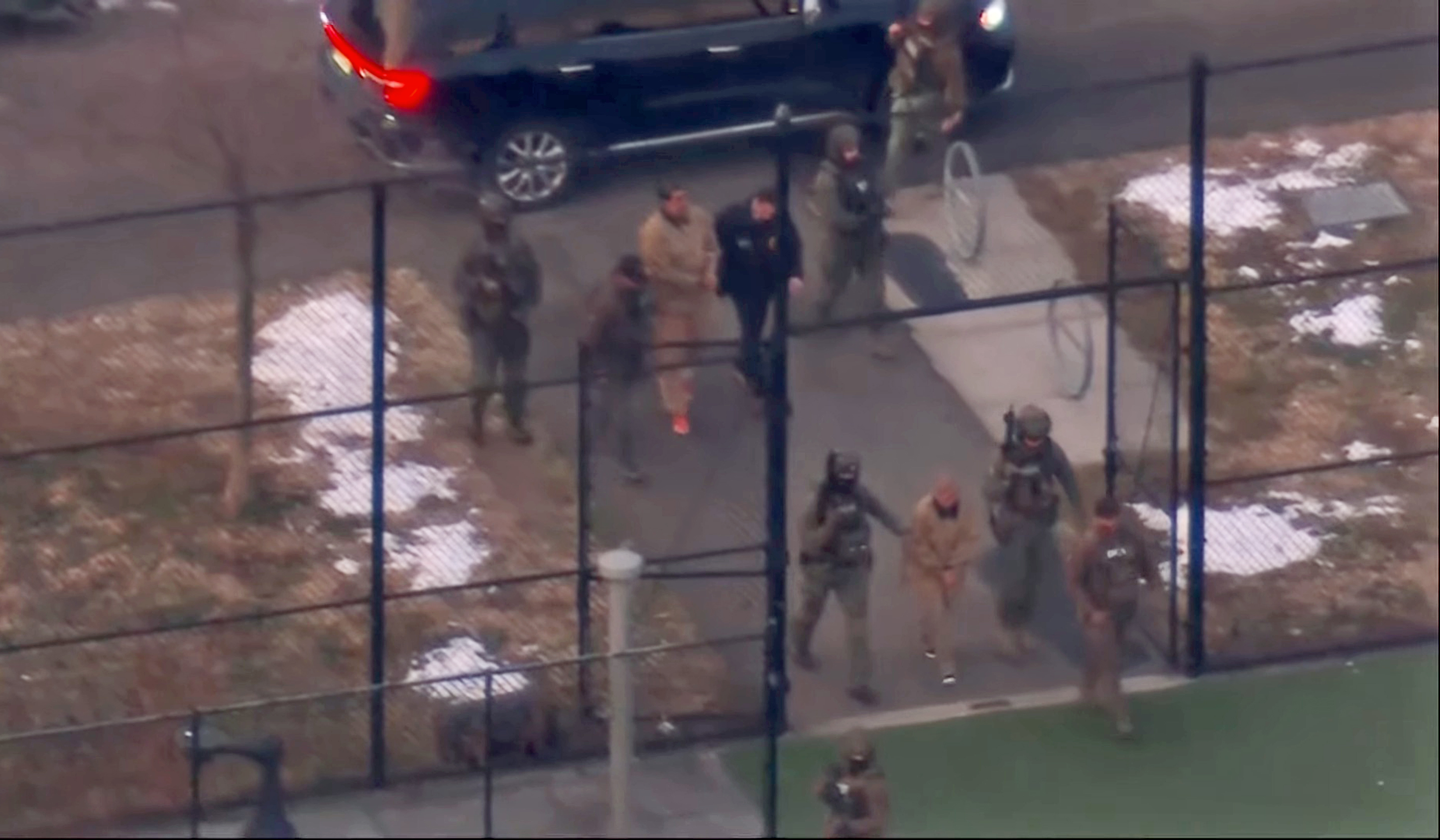 Aerial view of Venezuelan President Nicolas Maduro in handcuffs, escorted by officers, being moved from one vehicle to another.