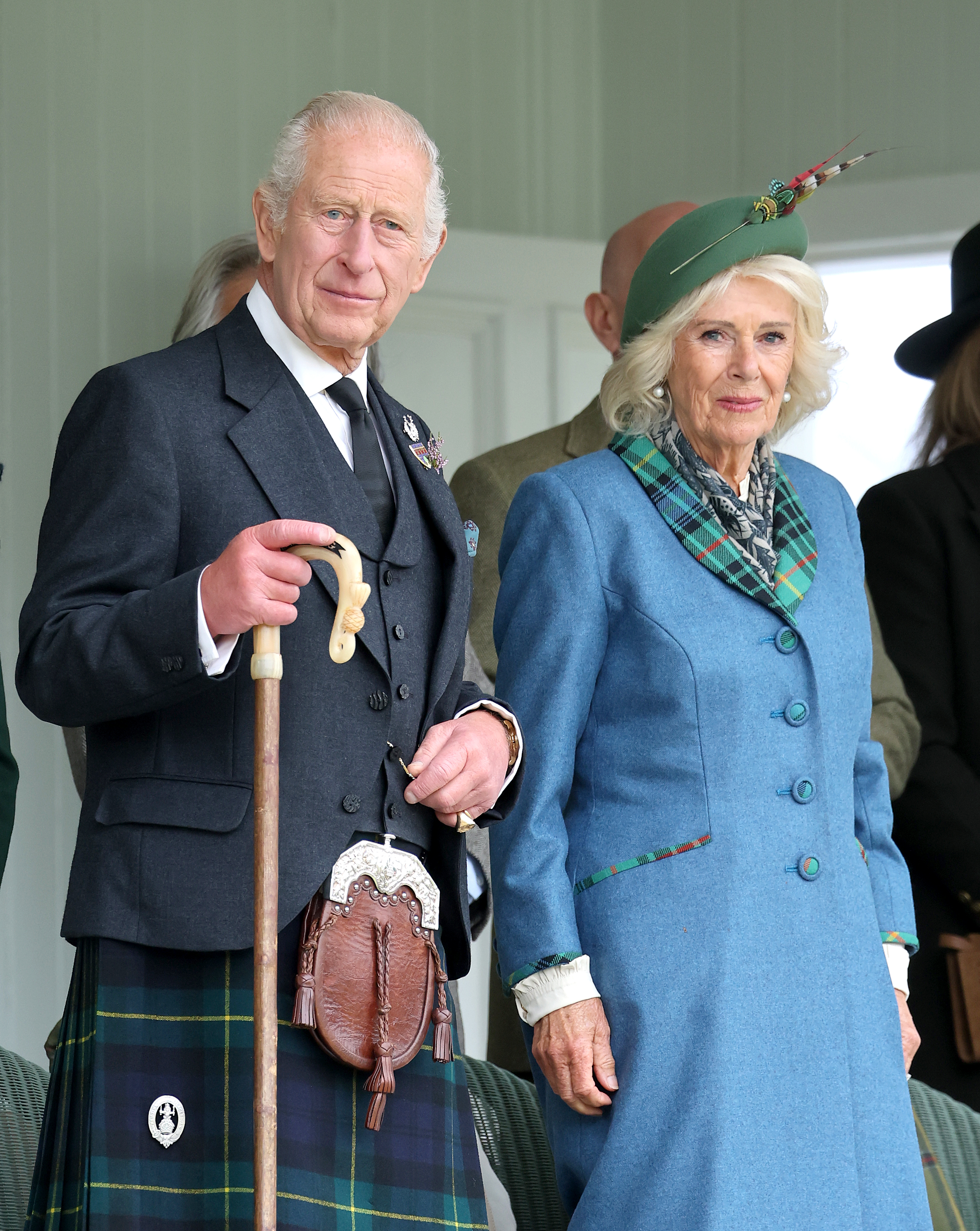 King Charles III, in a kilt, and Queen Camilla, in a blue coat and feathered hat, chat at the Braemar Royal Highland Gathering.
