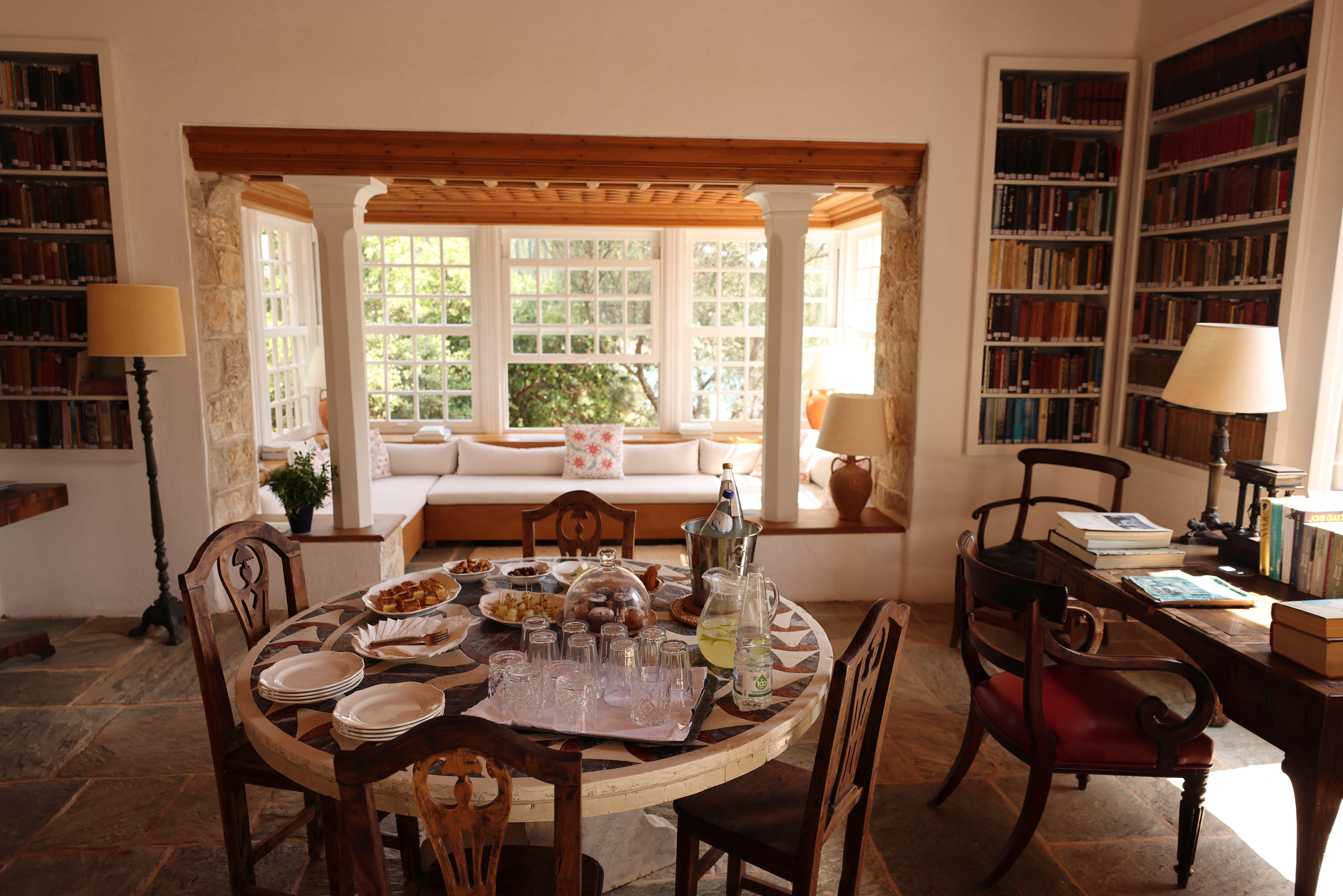 Indoor view of Patrick and Joan Leigh Fermor House, featuring a dining table with refreshments, a reading nook, and bookshelves.