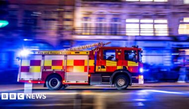 A fire engine drives on an urban road at night with blue lights on.