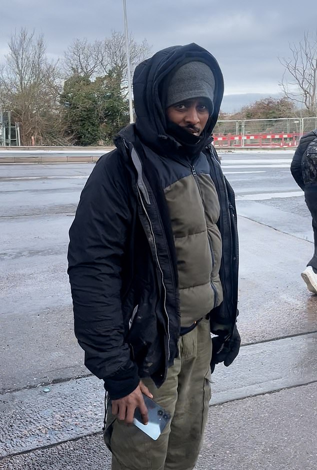 A migrant holds a phone as he looks at the lorry driver at the motorway station
