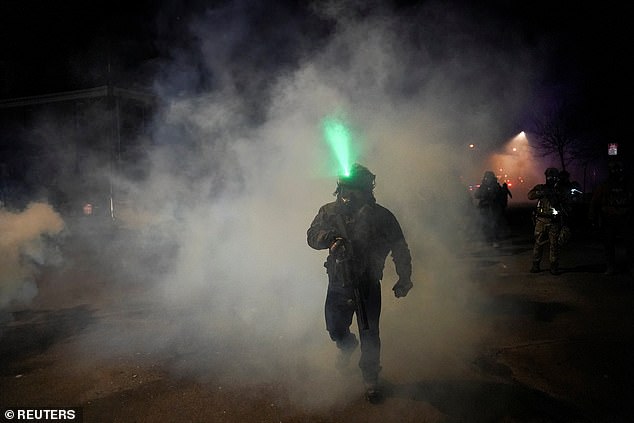 A federal agent walks through tear gas smoke after it was used on protesting community members
