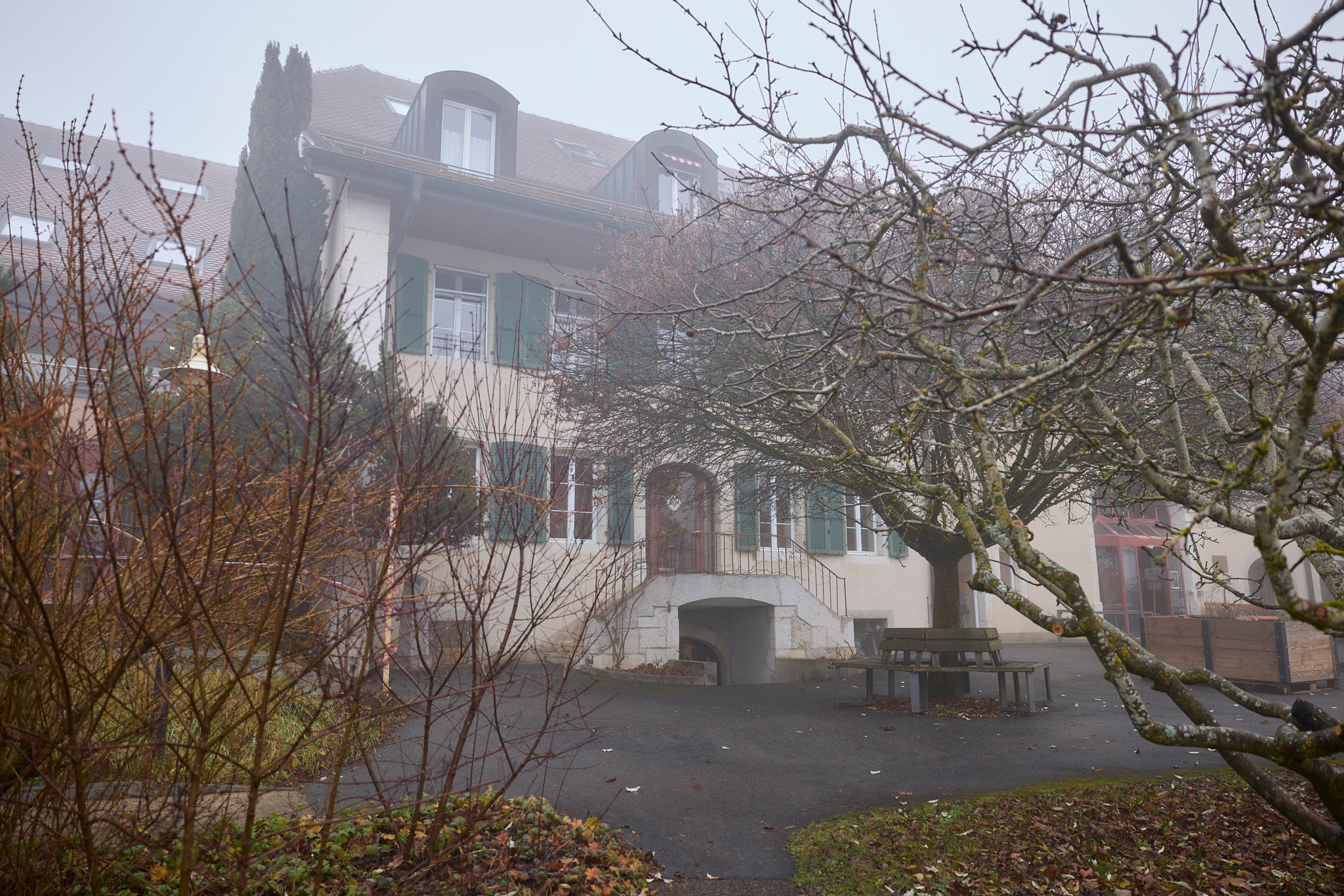 Le bâtiment principal de l’EMS Fondation Baud à Apples entouré de brouillard et d’arbres nus un jour d’hiver.
