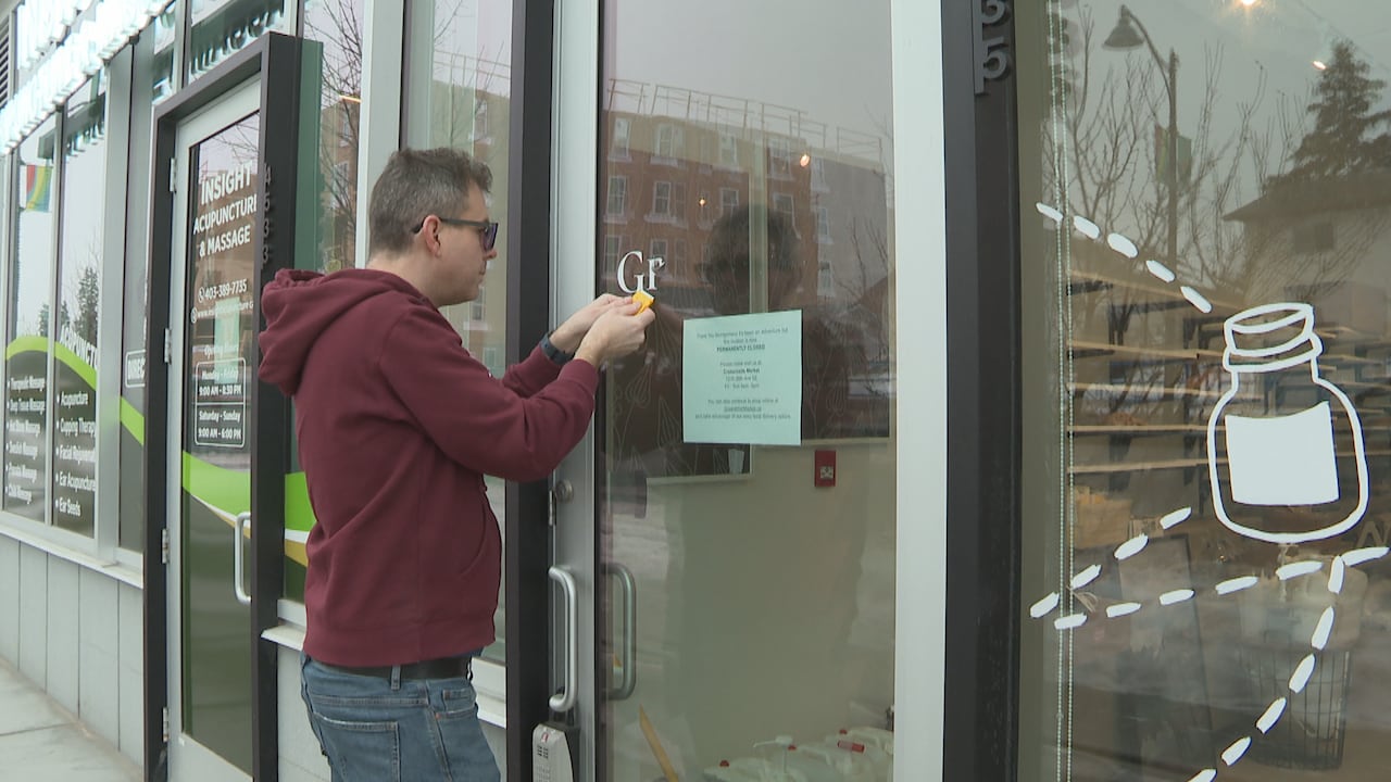 A man scrapes decal letters off of the window of a store door. 