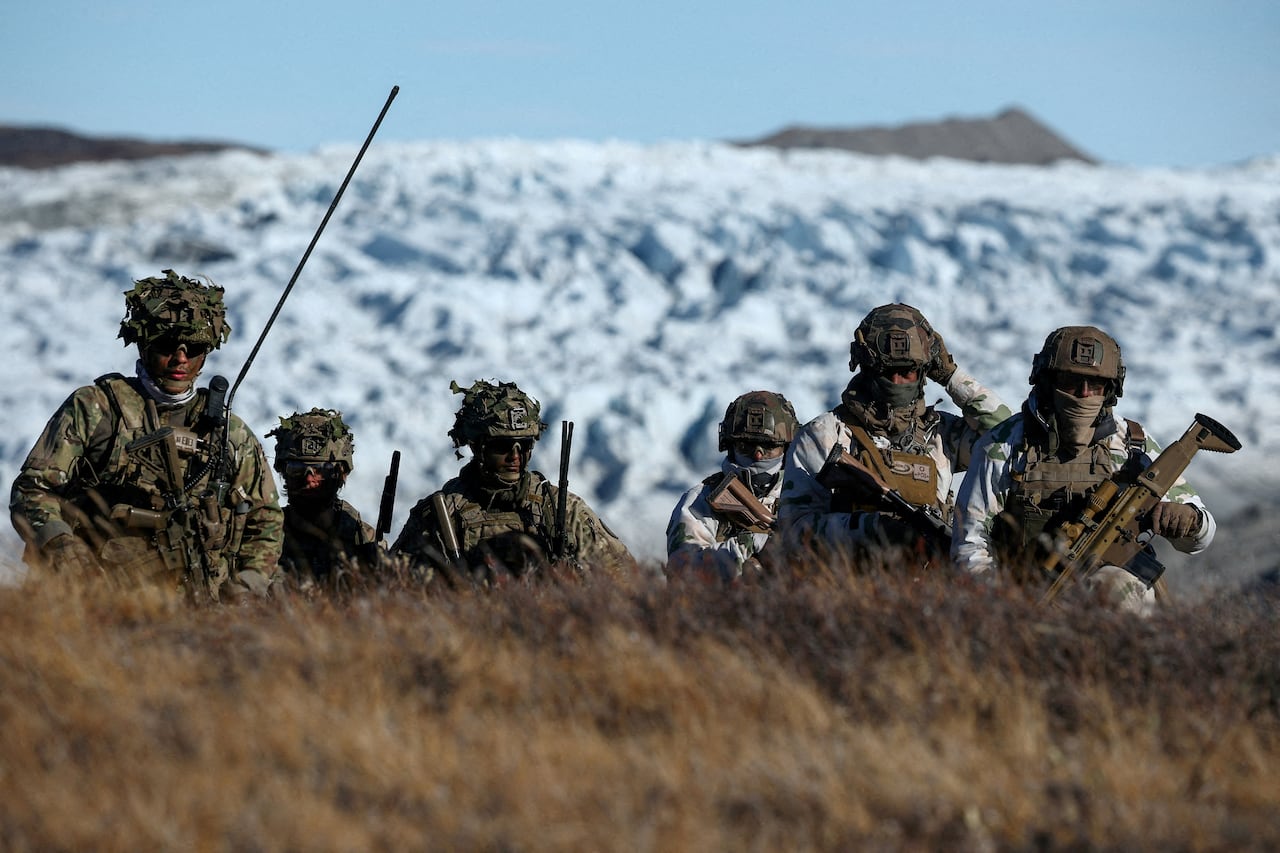 Armed soldiers in camouflage are shown above a rise, with snow behind them.