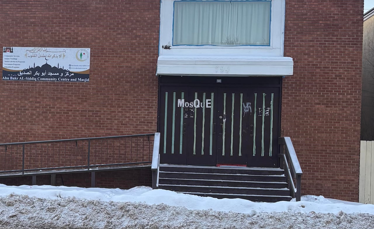 Swastikas are seen spray-painted on large wooden doors of a brick building.