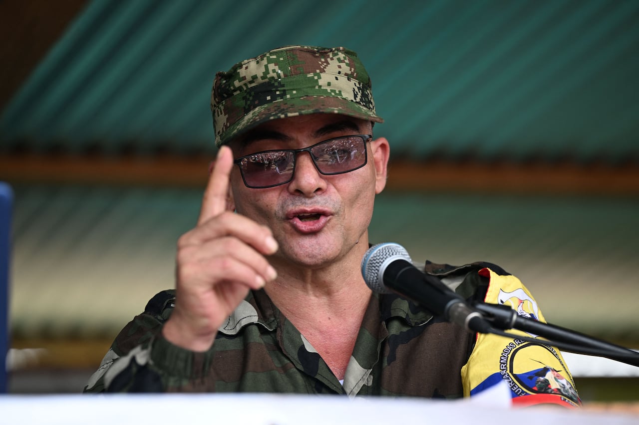 A man with sunglasses and a military cap gesturs with one finger.
