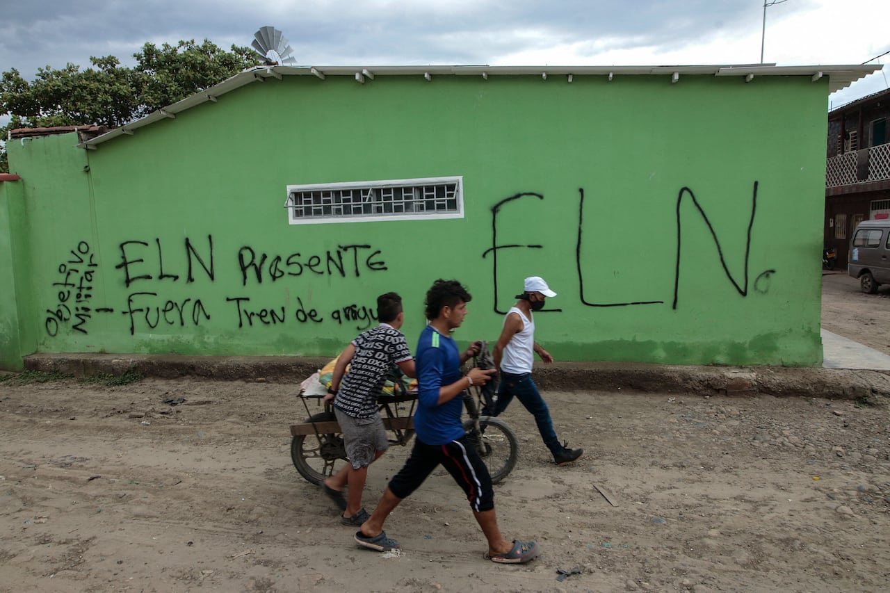 People walk by a wall with the spraypainted letters ELN. 