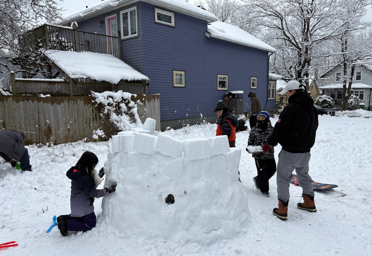 A group of kids pose with a half-built igloo made of snow.