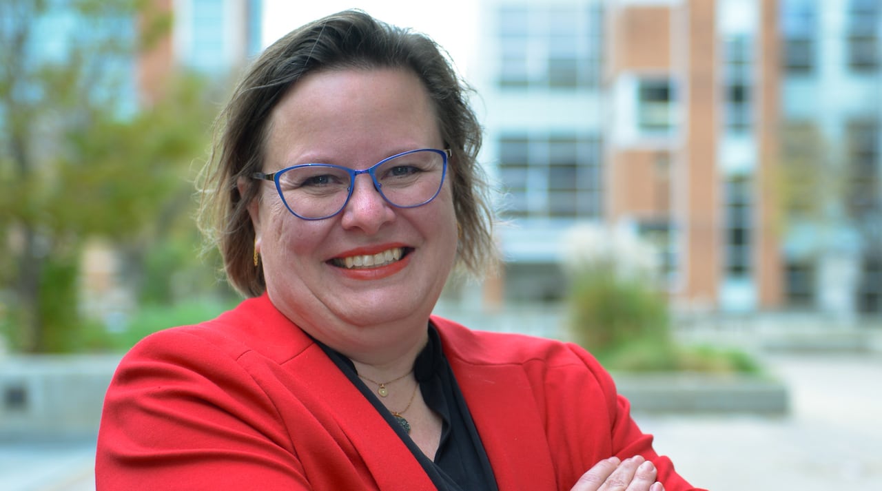 A woman in a red jacket, with arms folded in front of her, smiles at the camera.