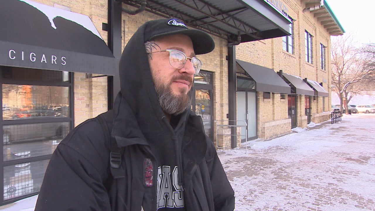 Man with a beard wears a eyeglasses and a black hooded sweatshirt under a black winter jacket