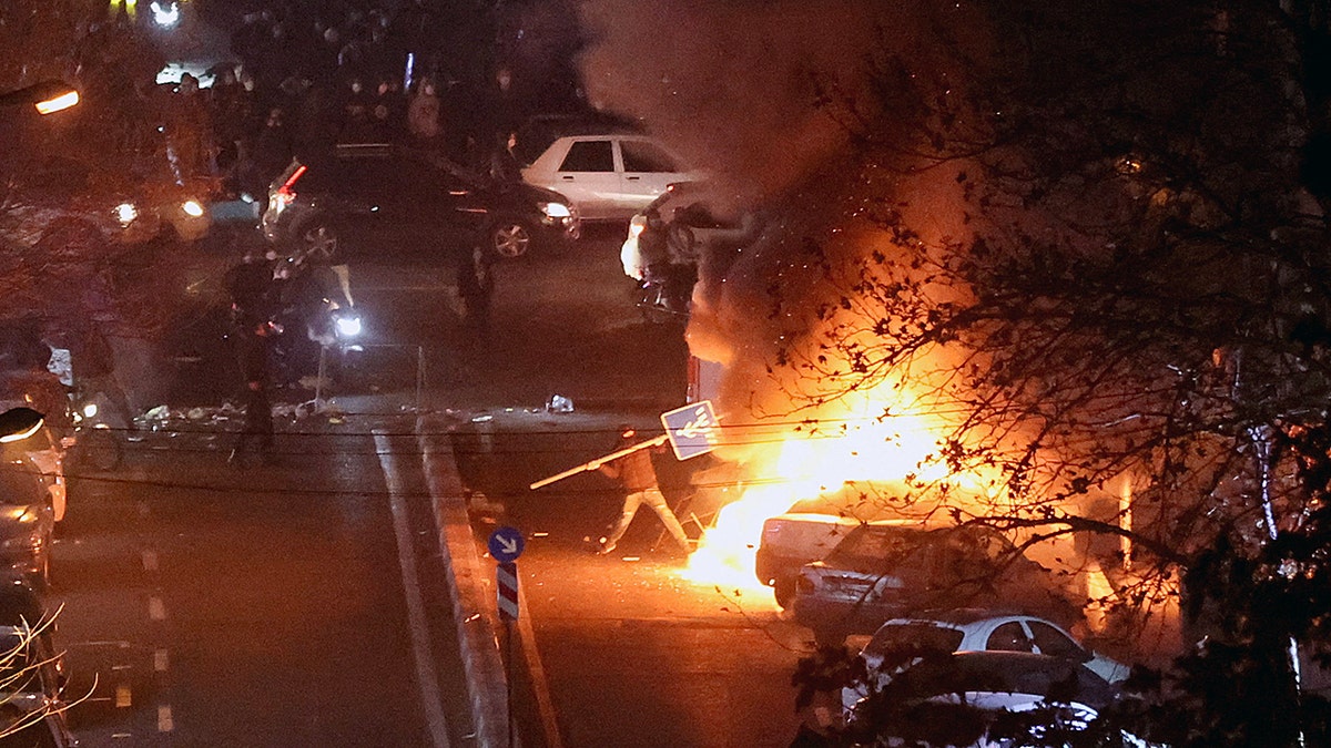 Iranian protester holds sign near fire in Tehran