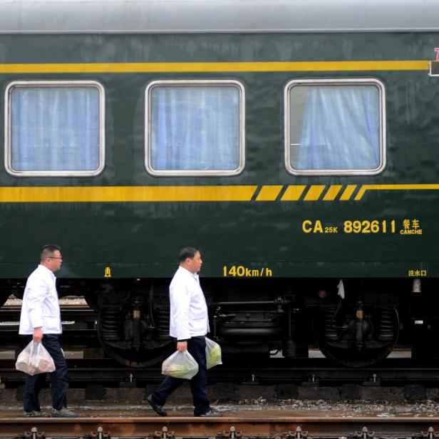 Drei Männer in weißen Hemden gehen mit Einkaufstüten an einem Zug entlang.