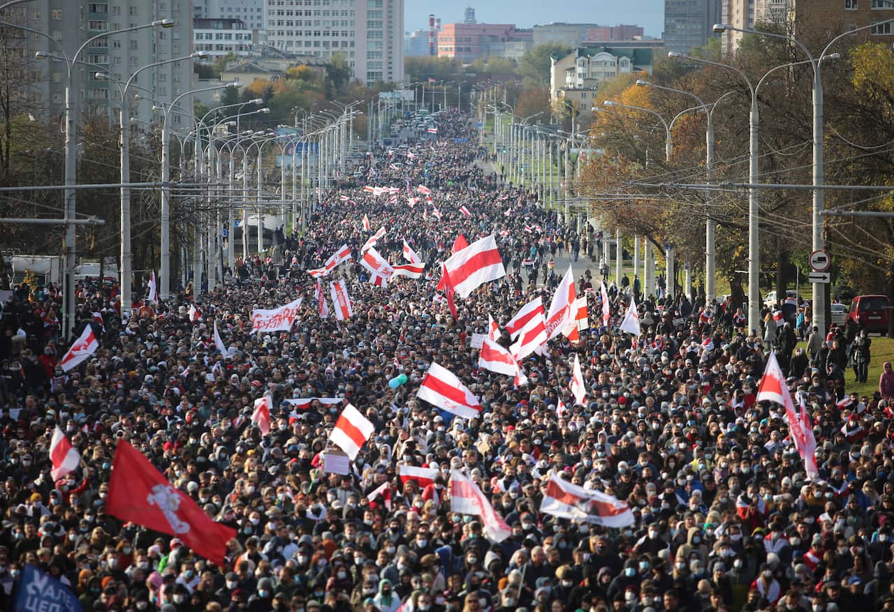 A massive crowd of people, many holding red-and-white flags, fills a wide city avenue stretching toward distant buildings.